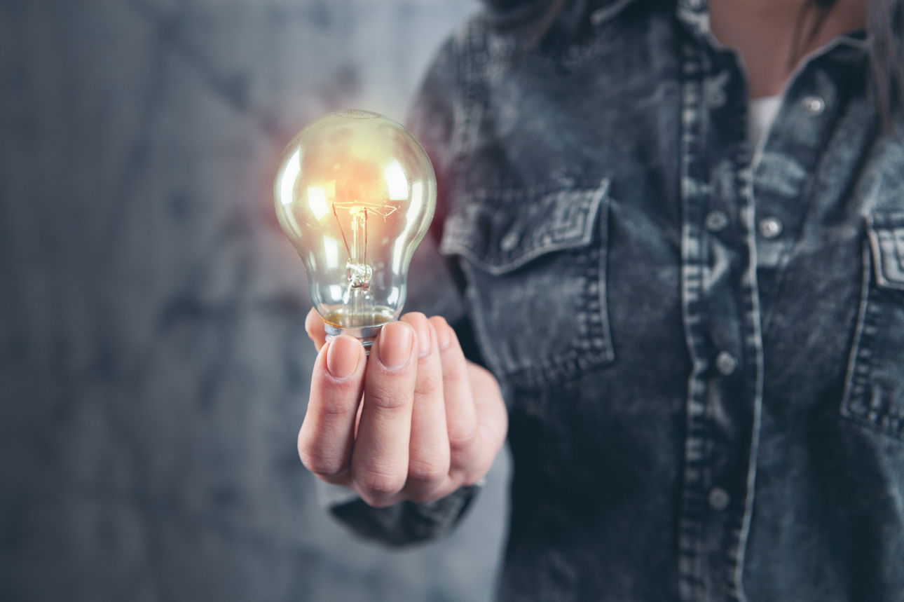 Woman in denim shirt holds lighted light bulb